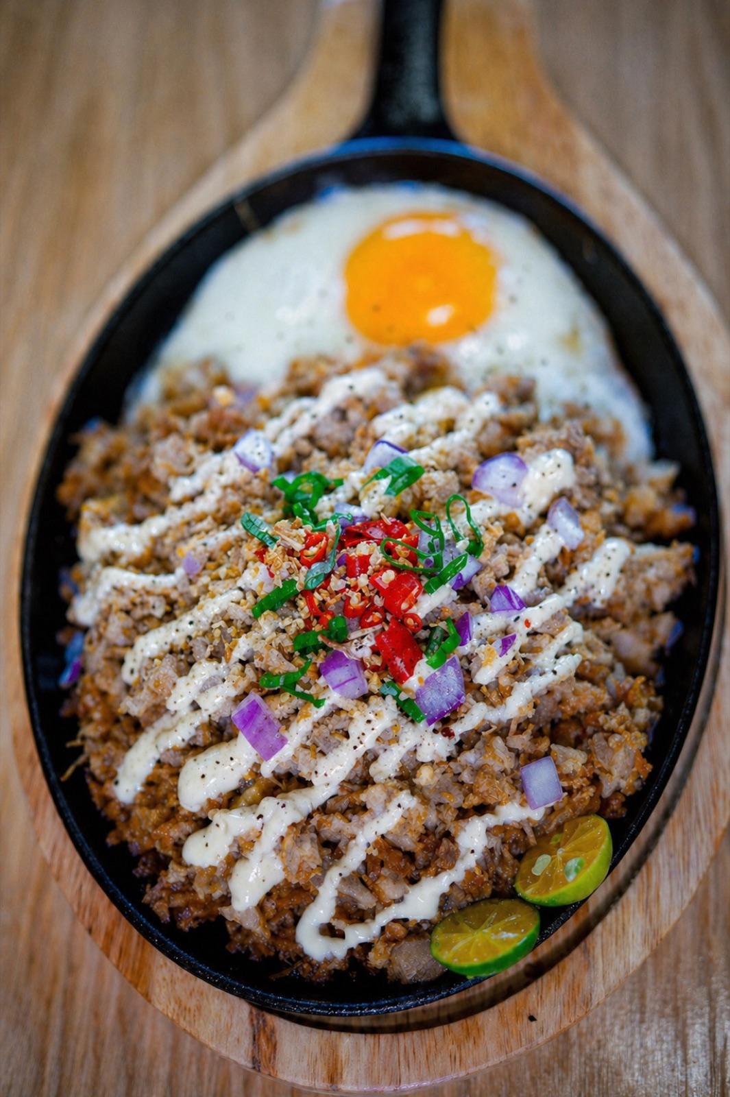Crispy pork sisig sizzling on a cast-iron plate with a sunny-side egg on top.